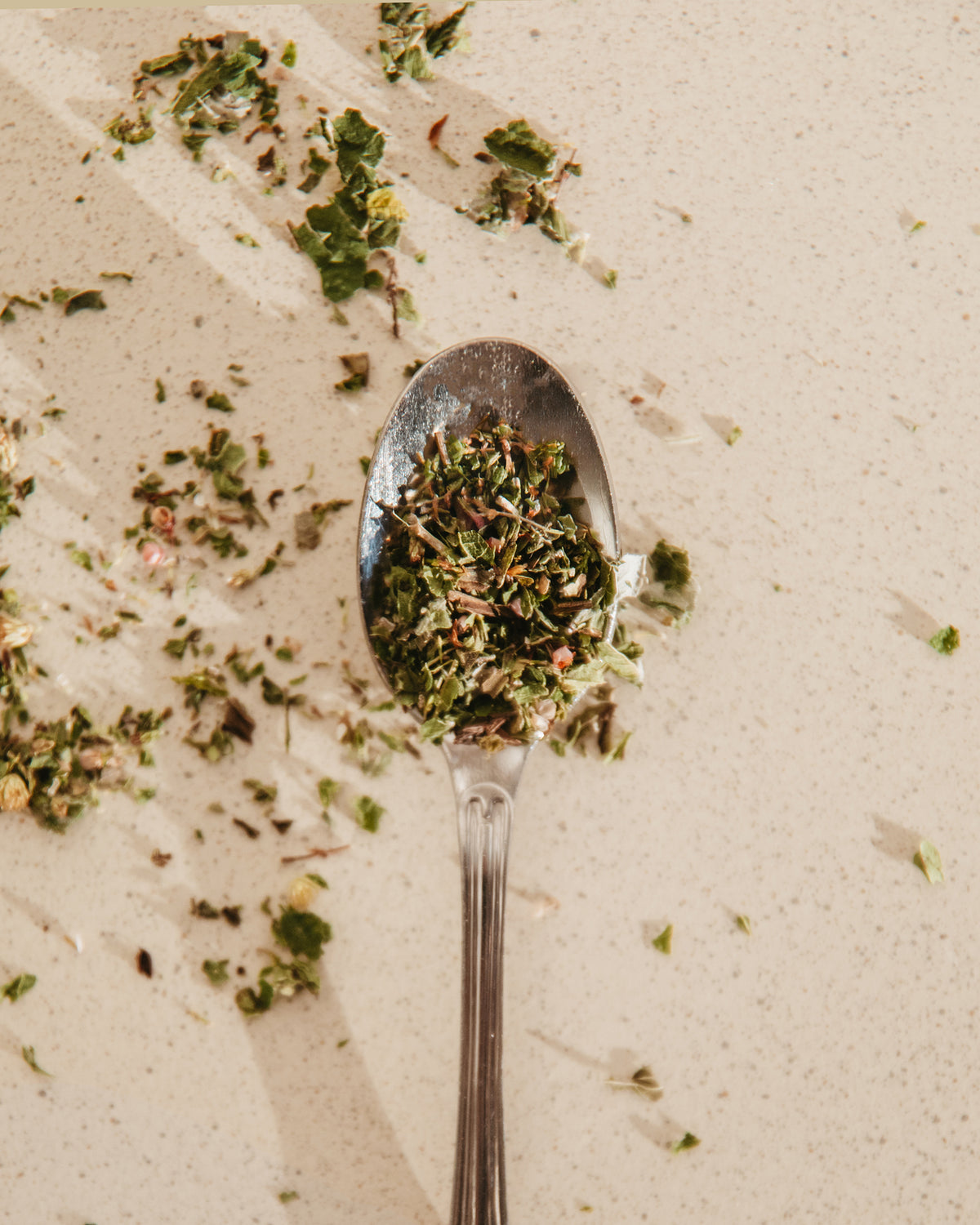 A spoon filled with loose Finnish herbal tea on a warm stone surface